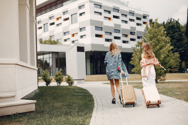 número de registro turístico Valencia España Madrid Barcelona. Rua, nrua, nra, registro de alquiler único ventanilla, teresa gestora de alquiler vacacional, colegio de registradores, turismo, vivienda uso turistico, vut, Airbnb, booking. Vbro. Pms. Dos mujeres con maletas entrando a un alojamiento turístico moderno EN: Two women with suitcases entering a modern tourist accommodation