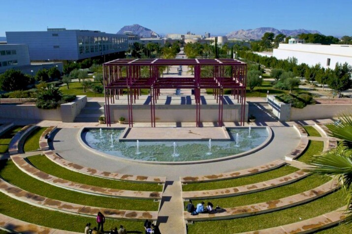 Número de Registro de Alquiler NRUA. Jornadas en la Universidad de Alicante. Panoramic view of a university campus with a central fountain and metallic structure.