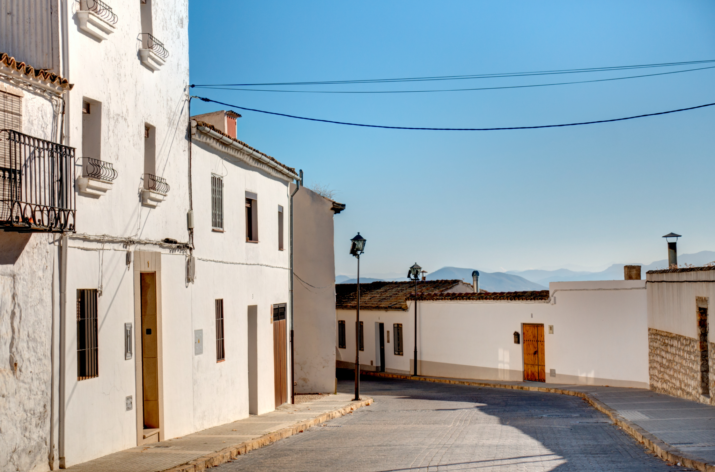 Rua, nrua, nra, registro de alquiler único ventanilla, teresa gestora de alquiler vacacional, colegio de registradores, turismo, vivienda uso turistico, vut, Airbnb, booking. Vbro. Pms. Calle empedrada en un pueblo rural con casas blancas y paisaje montañoso al fondo. Imagen de una calle empedrada en un pueblo rural, con casas blancas de estilo tradicional. Cobblestone street in a rural village with white houses and mountainous landscape in the background.